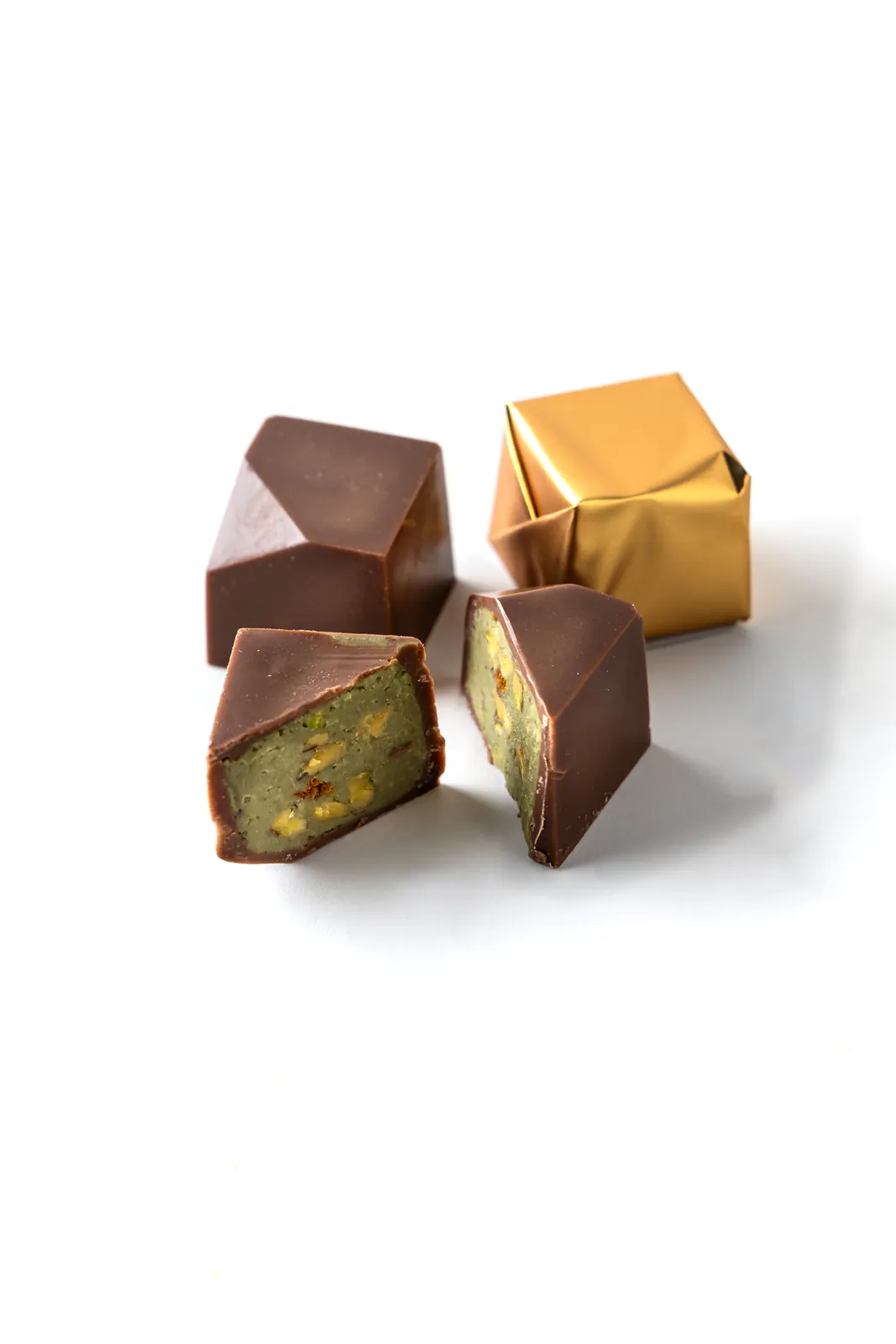 Faceted chocolate bonbons, one cut open to reveal a green pistachio filling